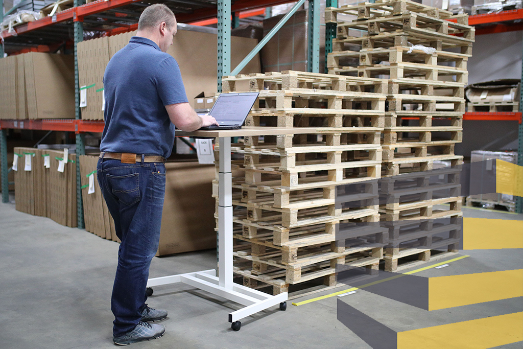 Man standing at computer desk to illustrate article on smart logistics warehouse. Photo by thestandingdesk on Unsplash.